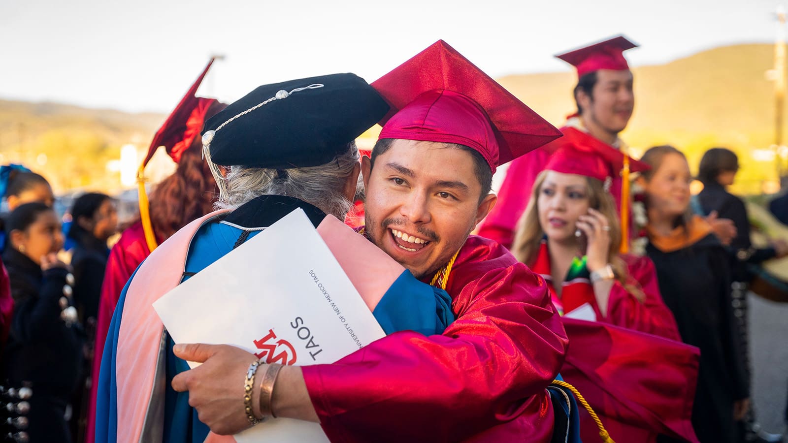 a graduate holding his diploma embraces a regent in graduation attire